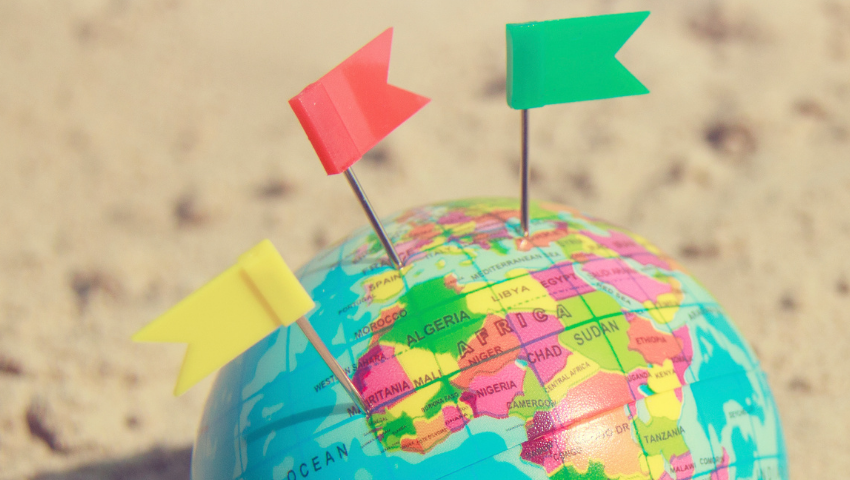 globe with yellow, red, and green flags sticking out of it resting in sand